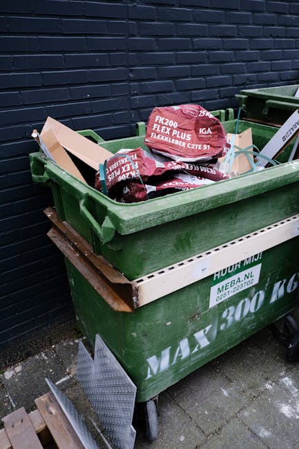 A collection of multiple large, transparent plastic bags filled with assorted waste materials, including clothing and packaging, piled on a brick pavement outside a commercial establishment. Behind th